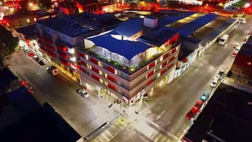 A multi-story hotel with a rooftop terrace, parking area, and adjacent buildings.