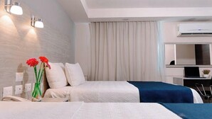 Hotellihuone, jossa on kaksi sänkyä, työpöytä kannettavalla tietokoneella, ilmastointilaite ja verho.