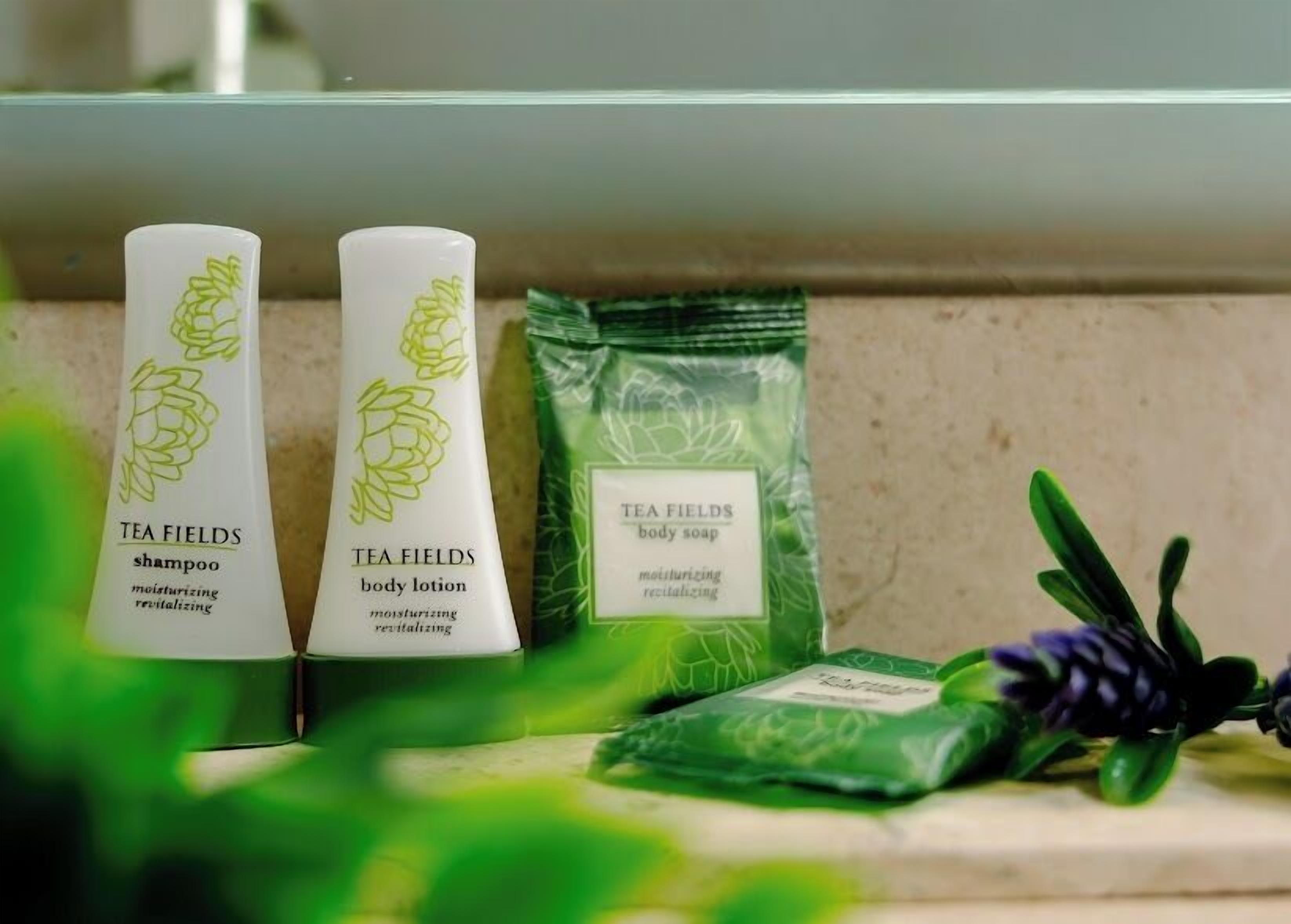 Two bottles of tea fields body lotion and shampoo, and a packet of tea fields body soap on a countertop.