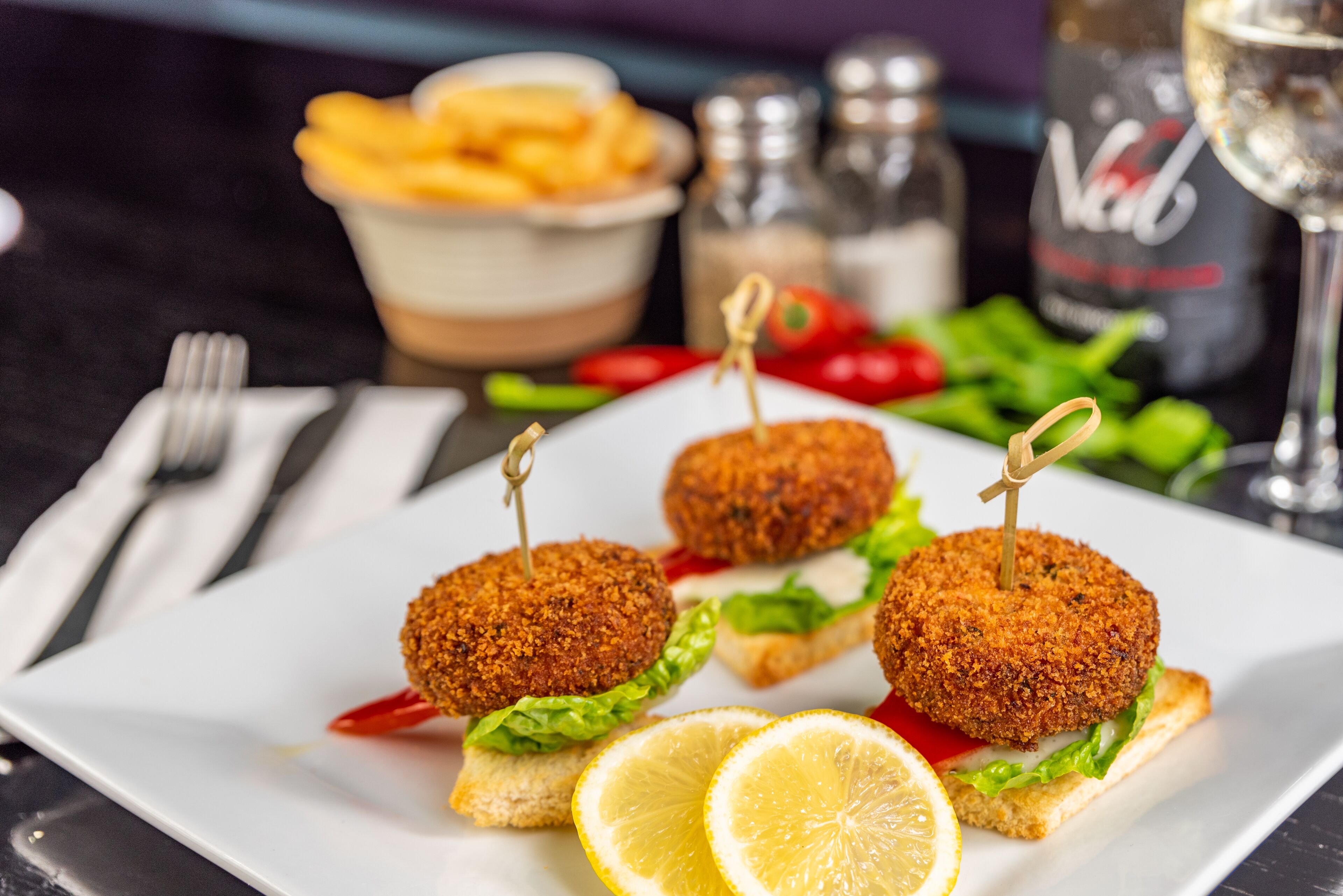 A plate with three breaded items on a white plate, garnished with lettuce and lemon slices.