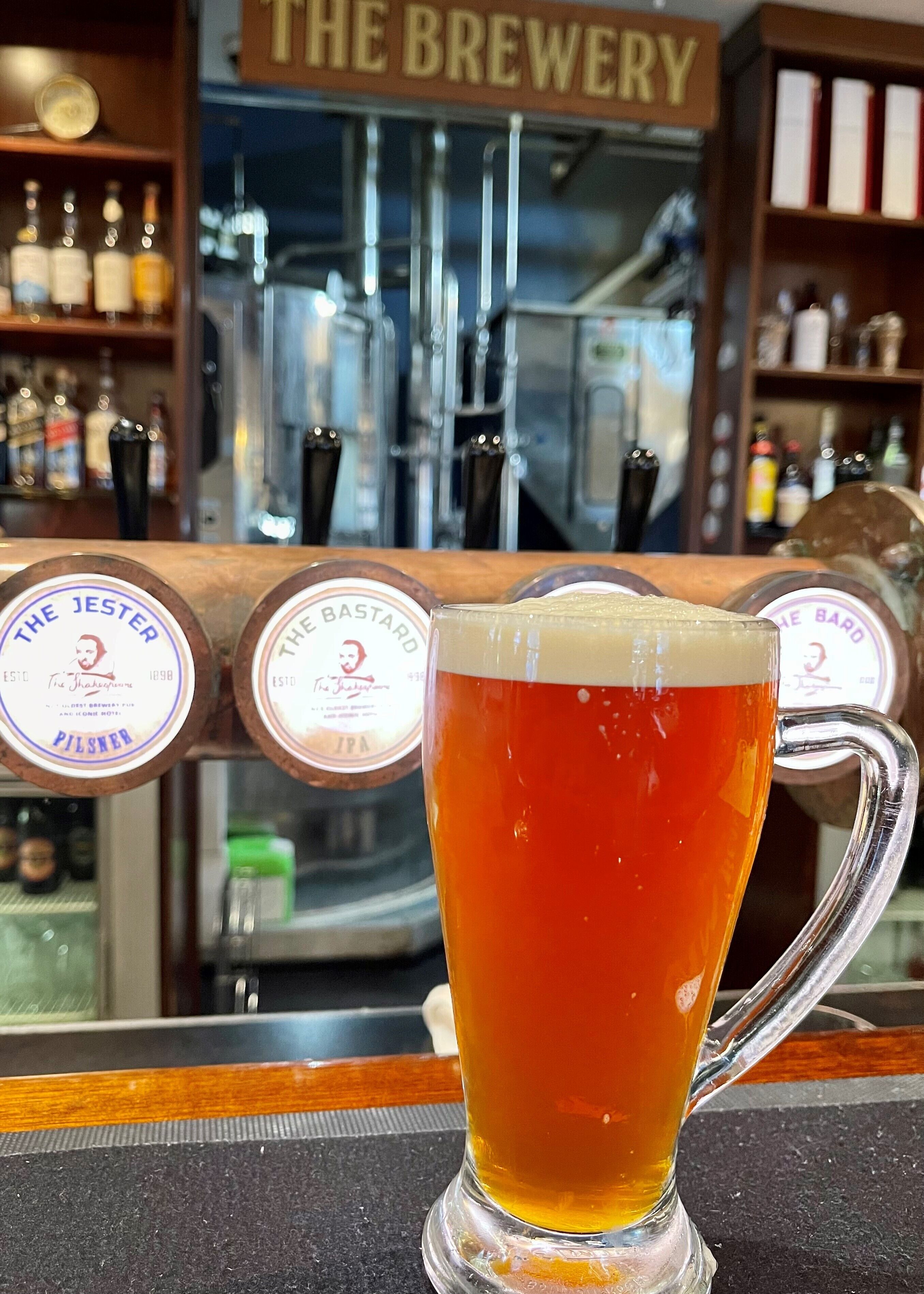 A glass of beer at a bar with taps labeled "The Jester," "The Bastard," and "The Bar."