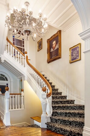 A grand staircase with ornate railings and patterned carpet, leading to a landing with a chandelier and framed artwork. - The Shakespeare Hotel (Auckland)