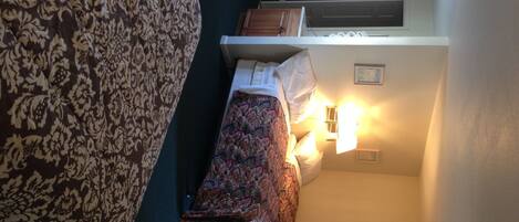 Een slaapkamer met een bed met een patroon, een nachtkastje met een lamp en een raam met uitzicht.