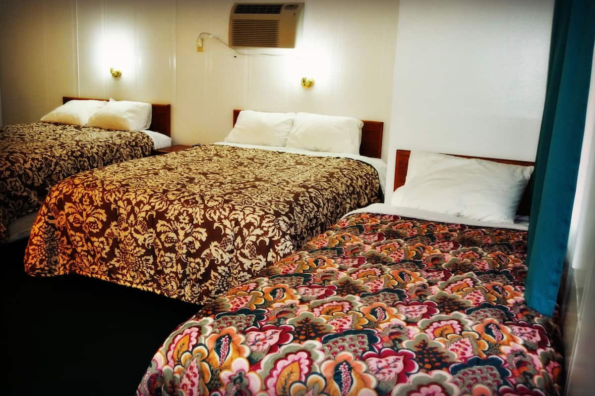A hotel room with two beds, each with patterned bedding, a wall-mounted air conditioner, and two wall-mounted light fixtures.