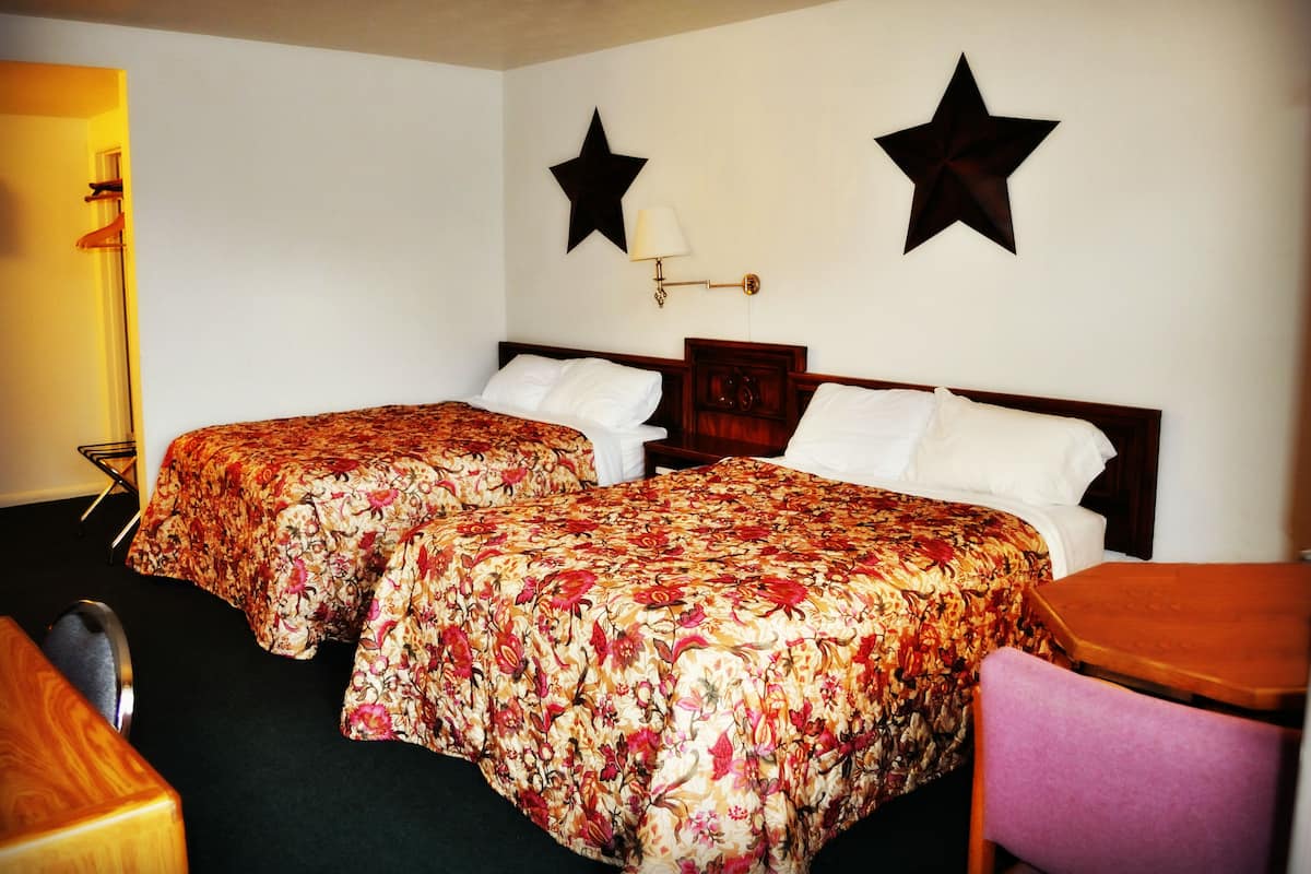A hotel room with two beds, a wooden nightstand, a chair, and two wall-mounted stars.