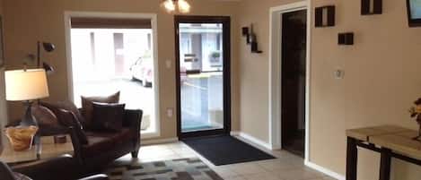 A living room with a sofa, a coffee table, a lamp, a patterned rug, a ceiling fan, and a door leading to a garage.