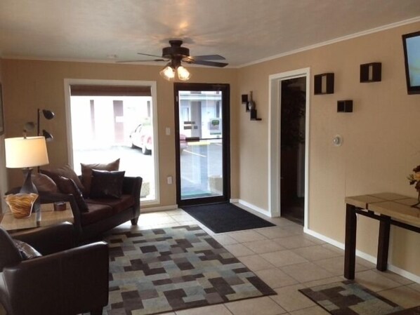A living room with a sofa, a coffee table, a lamp, a patterned rug, a ceiling fan, and a door leading to a garage. - Town House Motel (Rapid City)