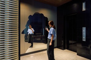A hotel lobby with a large mirror reflecting a person taking a photo. The hotel name 'HOTEL GRANDBACH SELECT KYOTO' is visible on the wall. - Hotel Grand Bach Kyoto Select (Kyoto)