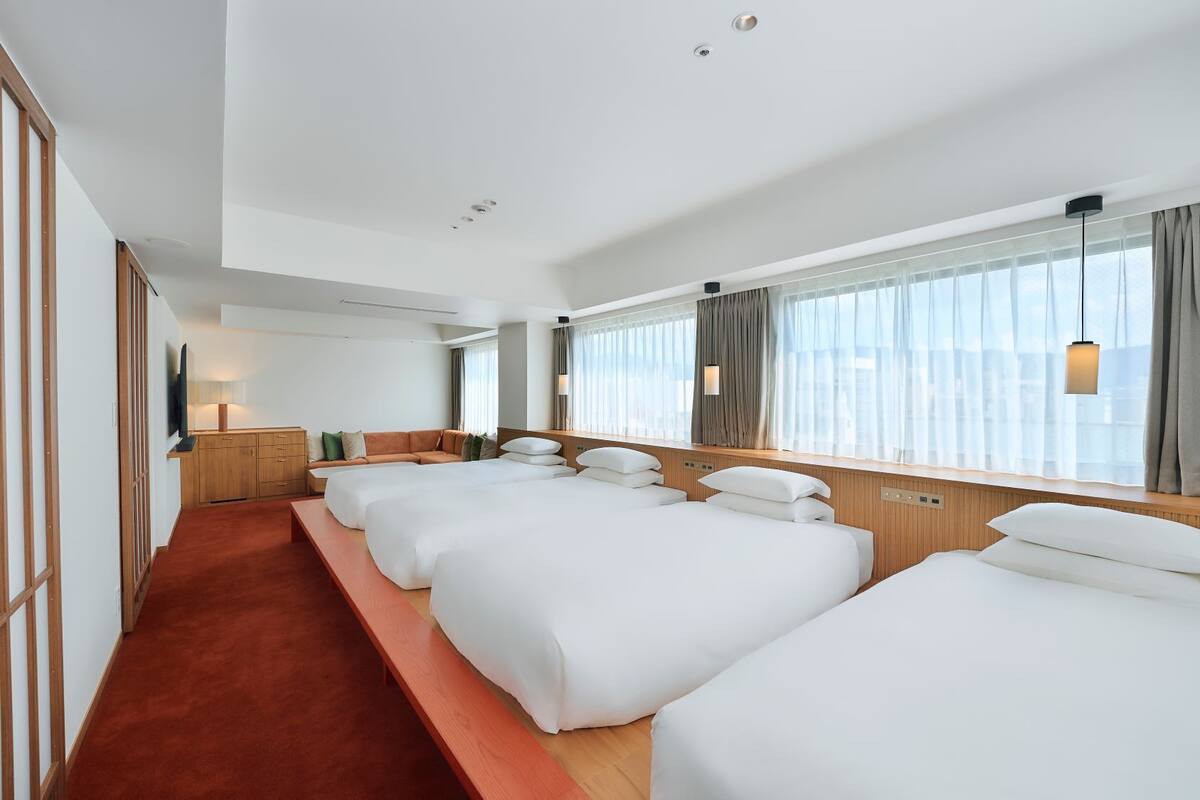A hotel room with a long corridor, multiple beds, a TV, and a window with curtains.