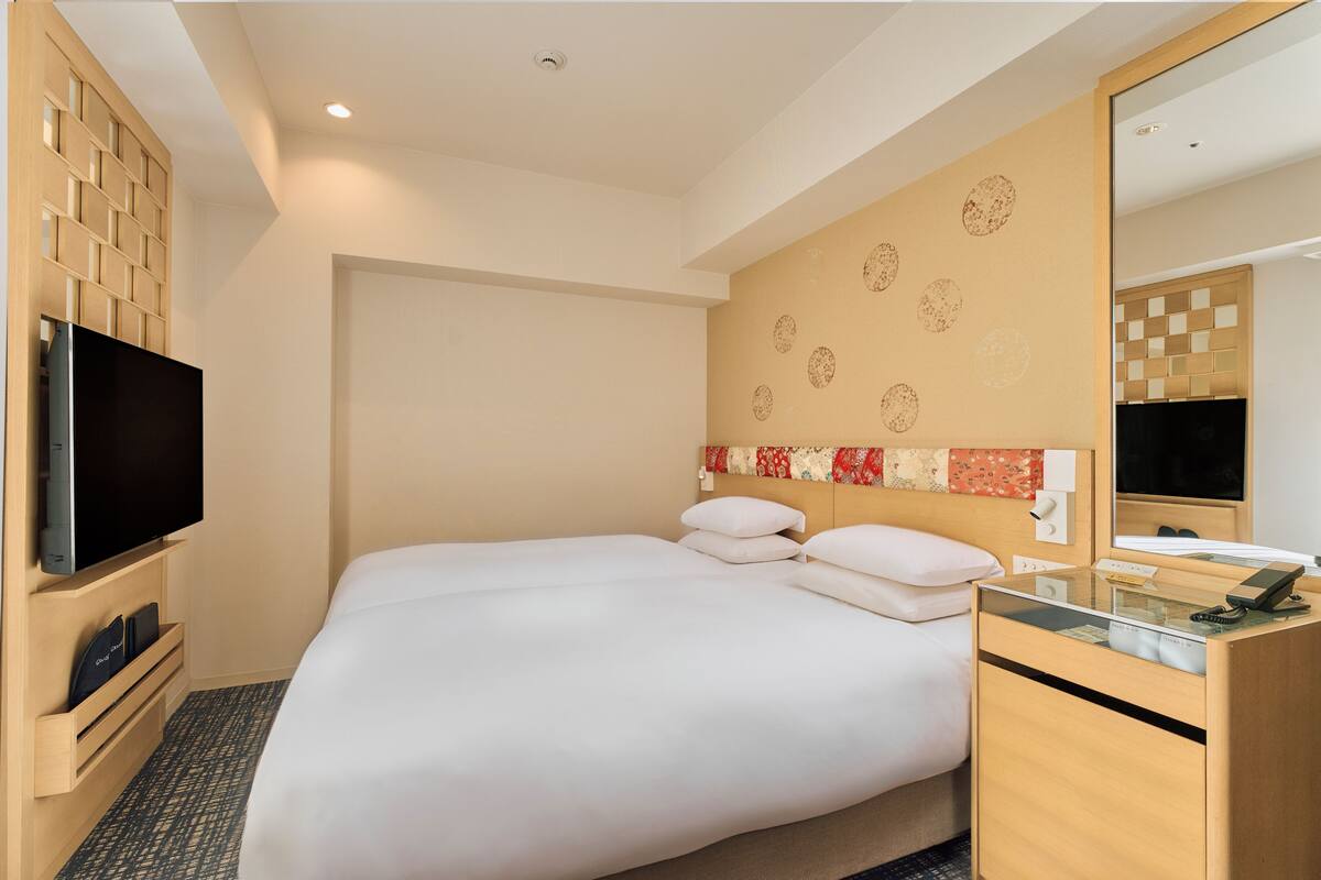 A hotel room with a large bed, a TV, a wooden dresser, and a mirror.