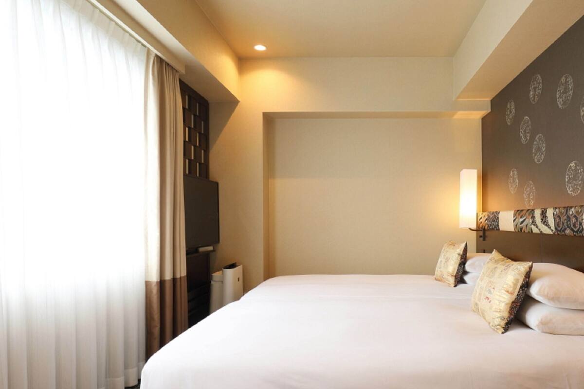 A hotel room with a large bed, a flat-screen TV, a bedside table, and a wall-mounted light fixture.