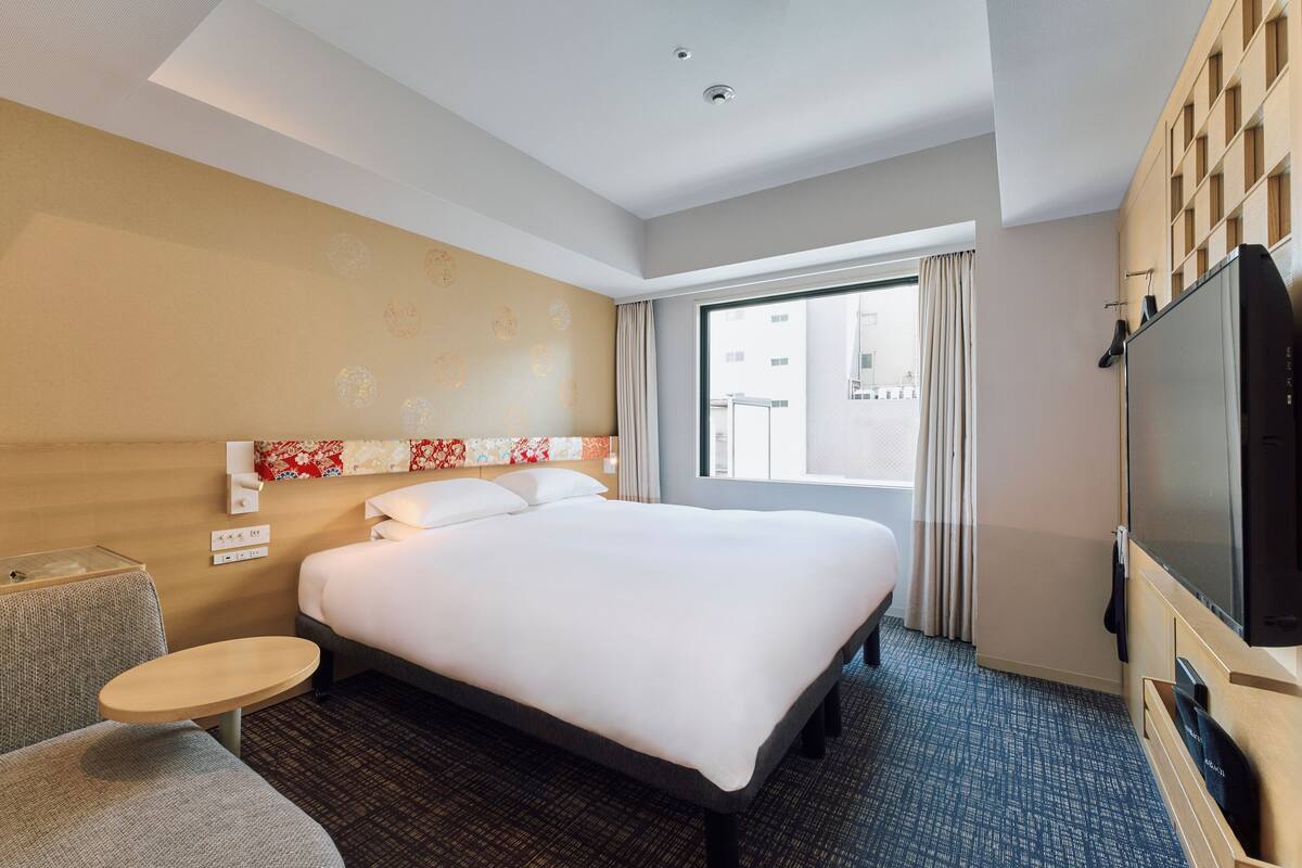 A hotel room with a large bed, a small round table, a TV, and a window with curtains.
