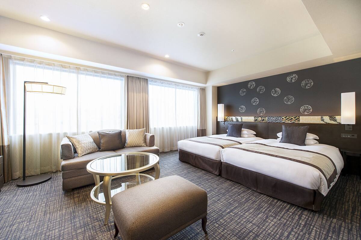 A hotel room with a sofa, a bed, a round table, and a large window with curtains.