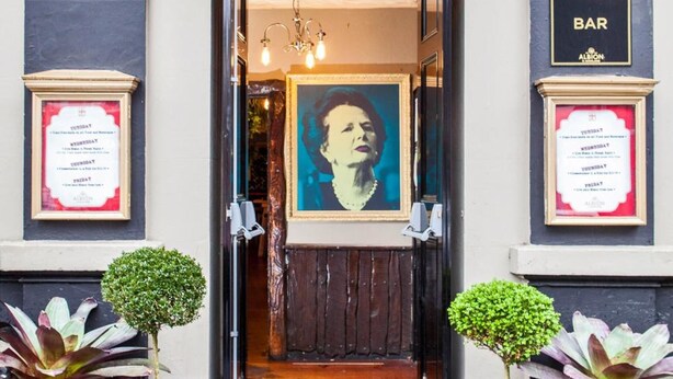 The entrance to the Albion of Auckland bar, featuring a classic architectural design with a black and white facade, framed artwork, and potted plants. - Albion of Auckland (Auckland)