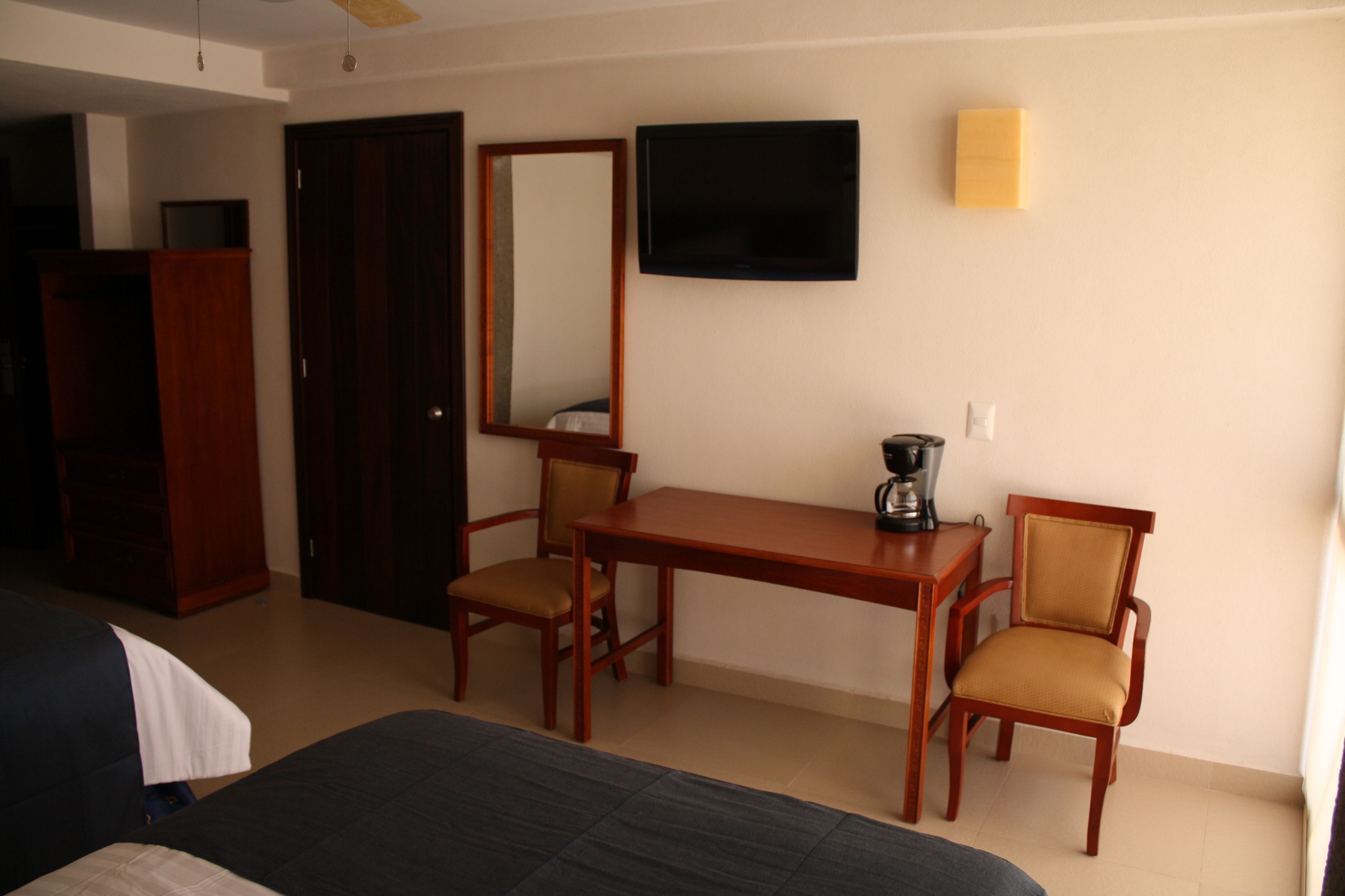 A hotel room with a bed, two wooden chairs, a table with a coffee maker, a TV, and a wardrobe.