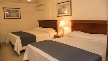 A hotel room with two single beds, a ceiling fan, a bedside lamp, and two framed pictures on the wall.