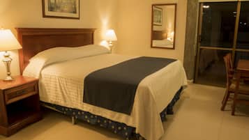 Habitación de hotel con una cama grande, dos lámparas de noche, una mesita de noche, una silla y un puerta corredera de vidrio que da a un balcón.