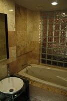 A bathroom with a glass-enclosed bathtub, a glass sink, and a marble-tiled wall.