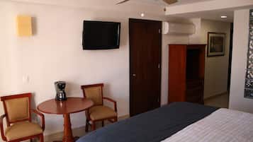 A hotel room with a bed, a television, a coffee maker, and a wooden wardrobe.