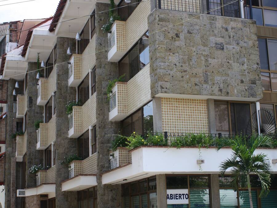 Un immeuble à plusieurs étages doté de balcons, une devanture visible avec une enseigne et une voiture garée.