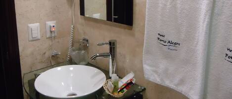 A bathroom with a glass sink, a hairdryer, a towel, and a toilet.