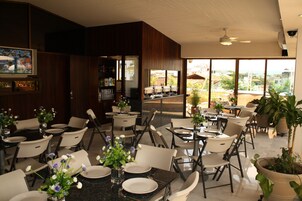A restaurant with multiple tables and chairs, a bar area, and large windows offering a view of the city.