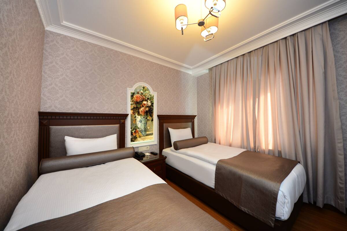 A hotel room with two beds, a nightstand, a lamp, and a painting on the wall.
