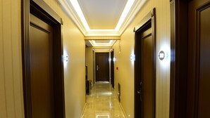 Un pasillo de hotel con puertas de madera, suelo de mármol y apliques de luz.