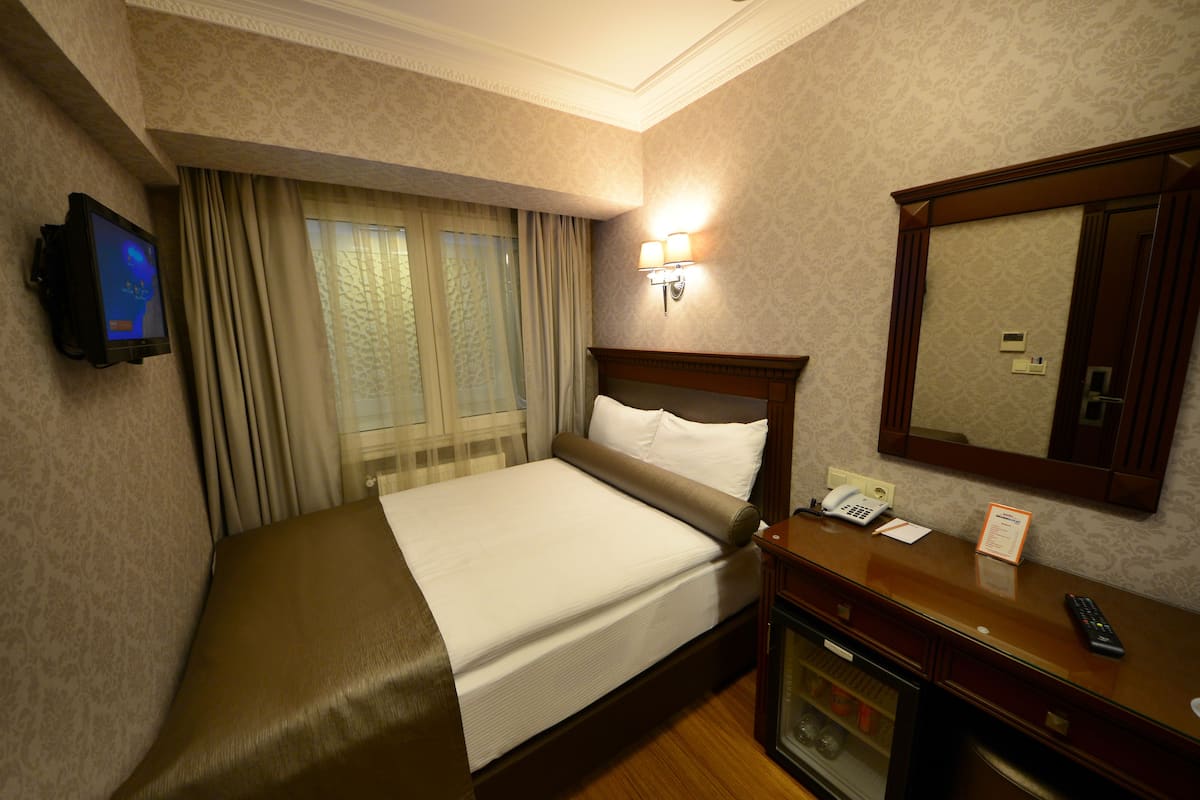 A hotel room with a bed, a television mounted on the wall, a bedside table with a phone and a remote control, and a mirror above the table.