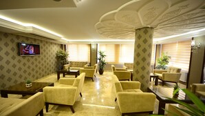 Vestíbulo de hotel de diseño moderno, con una zona de estar central con sofás y sillones, un televisor montado en la pared y columnas decorativas.