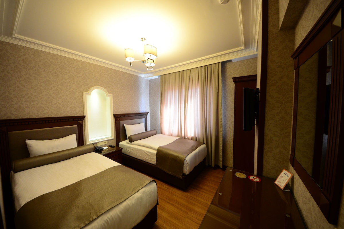 A hotel room with two beds, a nightstand, a mirror, and a window with curtains.