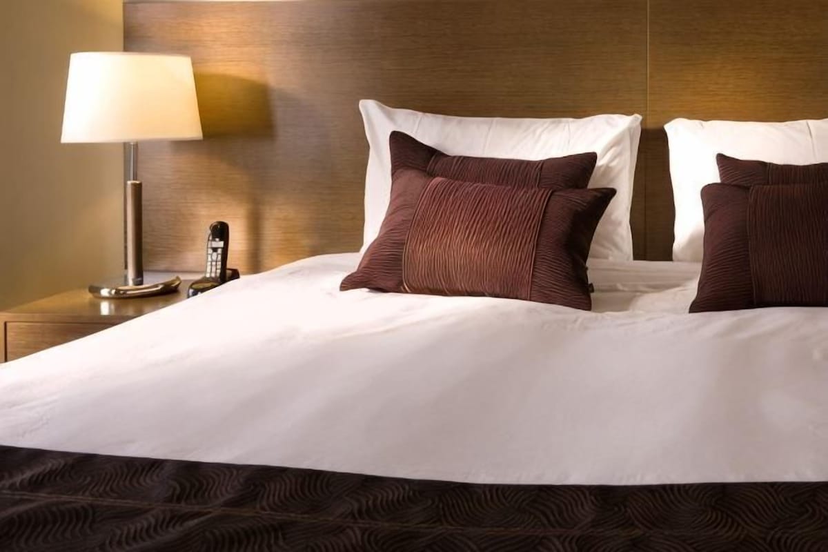 A hotel room with a large bed, a bedside lamp, and a telephone.