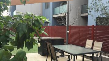 An outdoor patio area with a table and chairs, a barbecue grill, and a red fence.