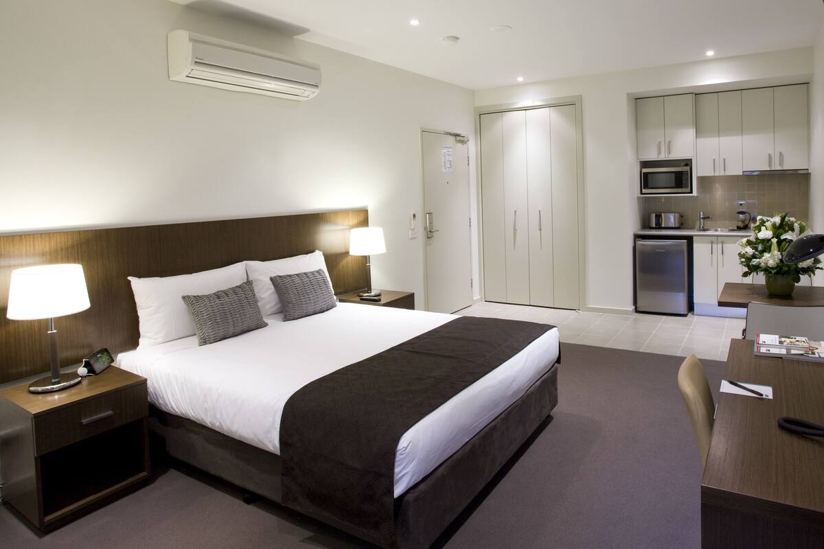 A hotel room with a large bed, bedside tables, a desk, a microwave, and a refrigerator.