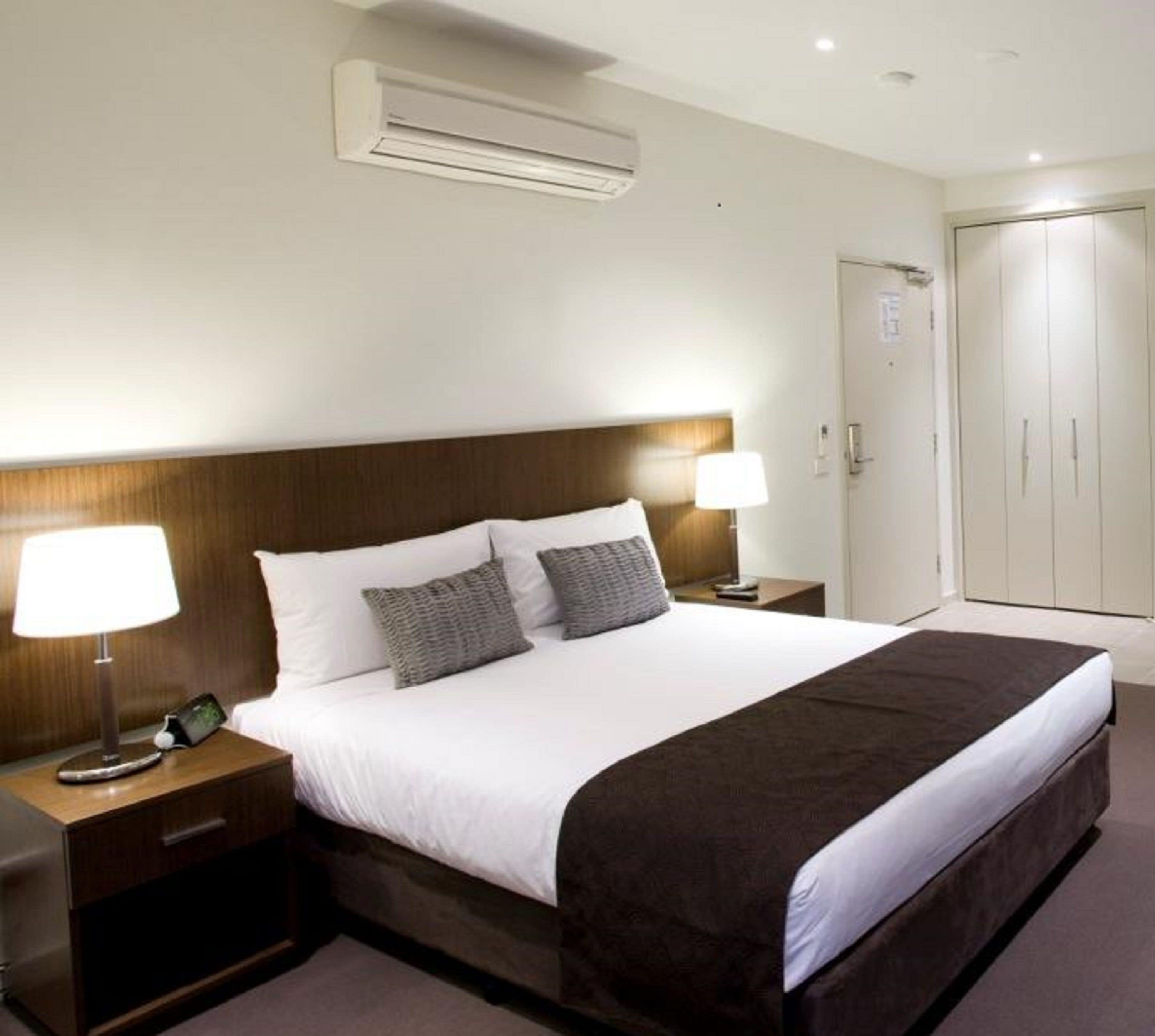 Une chambre d’hôtel avec un grand lit, deux tables de chevet avec des lampes, une armoire et un appareil de climatisation.