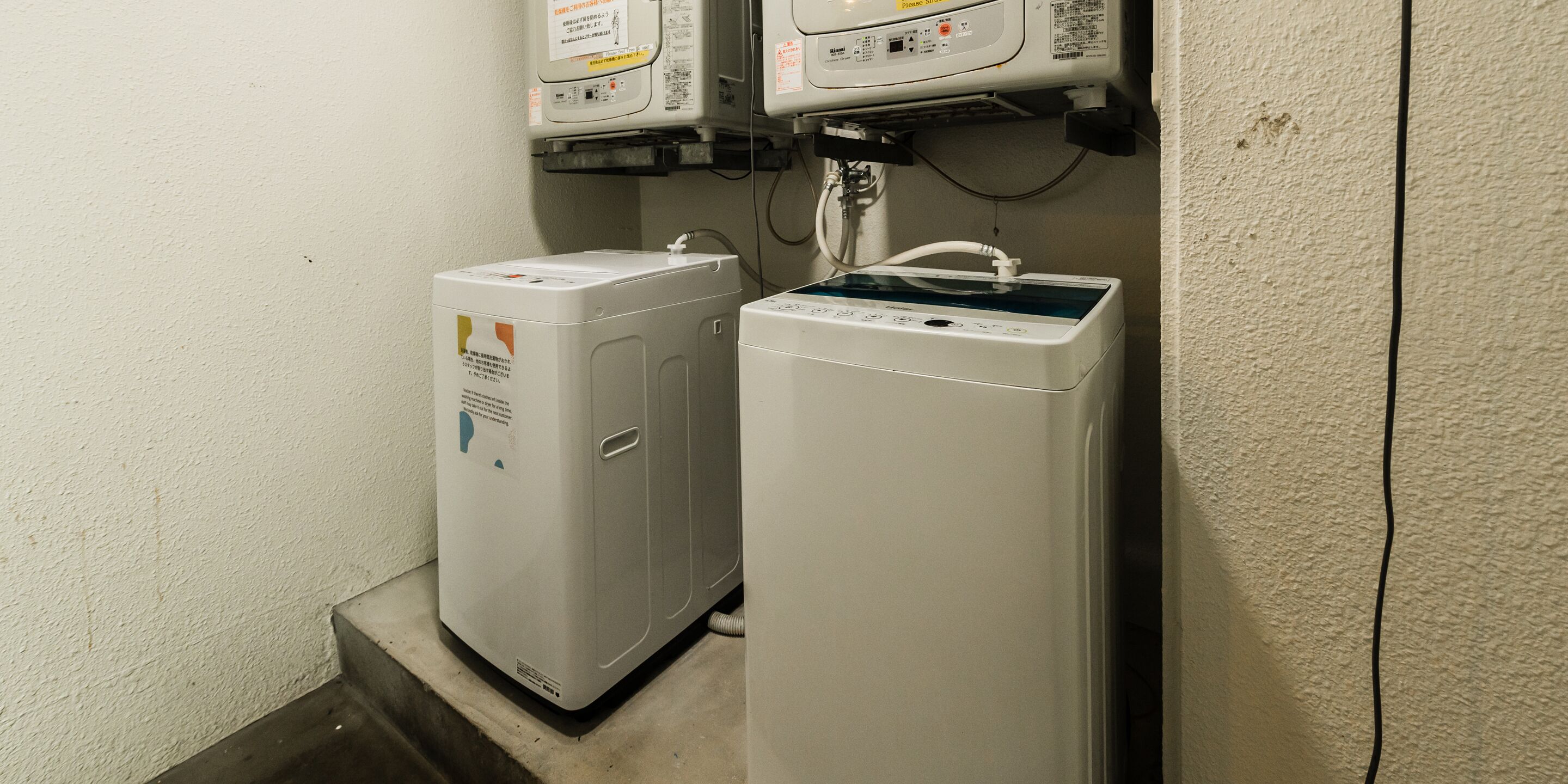 Two stacked laundry machines in a corner with a wall-mounted electrical panel above.