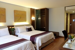 A hotel room with two beds, a wooden wardrobe, a desk with a tray of breakfast items, and artwork on the wall.