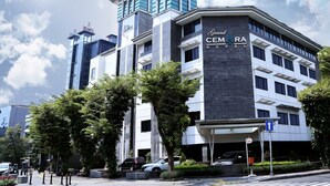 A modern hotel with a prominent 'Grand CEMARA HOTEL' sign, a parking garage, and a clear sky.