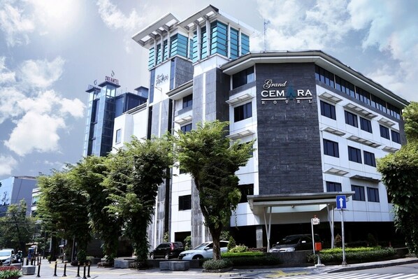 A modern hotel with a prominent 'Grand CEMARA HOTEL' sign, a parking garage, and a clear sky.