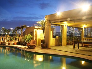 Zona de piscina con vista a la ciudad, mobiliario exterior e iluminada terraza.
