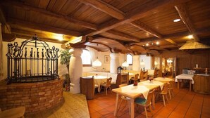 A rustic dining area with wooden tables and chairs, a brick fireplace, and exposed wooden beams on the ceiling. - Hotel Alter Hof (Vaterstetten)
