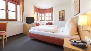 A hotel room with a bed, a desk with a lamp, a chair, a television, and a telephone. - Hotel Alter Hof (Vaterstetten)