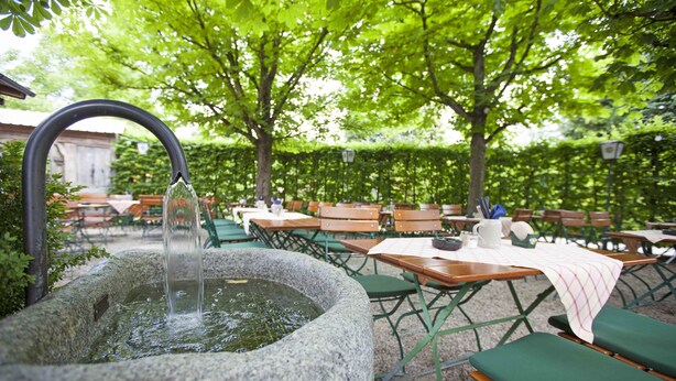 An outdoor seating area with stone planters, wooden tables, and green chairs. - Hotel Alter Hof (Vaterstetten)