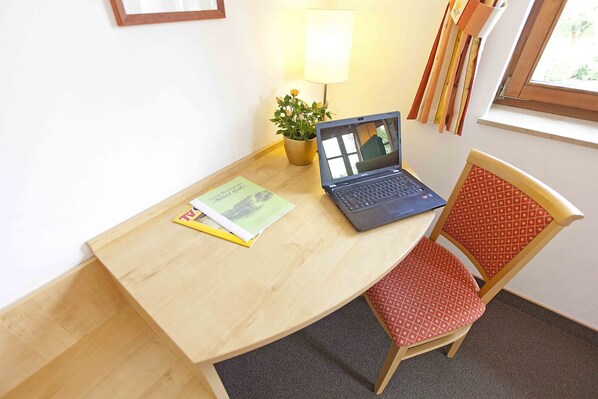 A wooden desk with a laptop, a plant, and a chair with a patterned cushion. - Hotel Alter Hof (Vaterstetten)