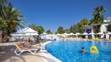 A pool area with lounge chairs and umbrellas, surrounded by palm trees and a clear blue sky.