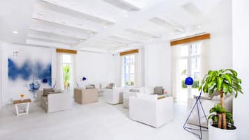 Un salon spacieux et moderne, doté de meubles blancs, de grandes fenêtres et d’un plafond avec des poutres apparentes.