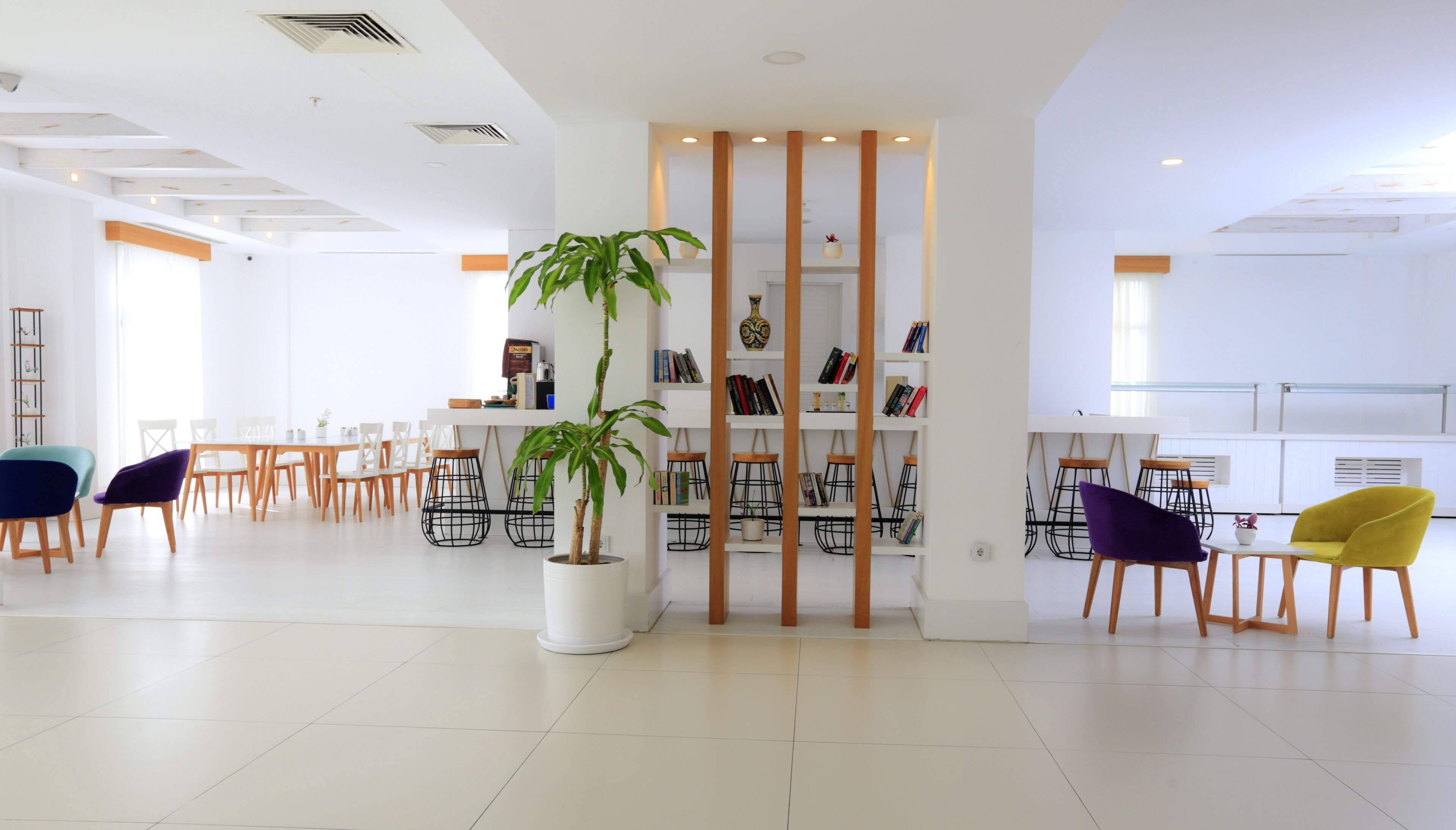 A spacious, well-lit lobby with a central plant, seating area, and a bookshelf.