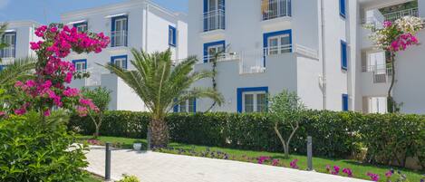 A modern building with balconies, a paved walkway, and lush greenery.