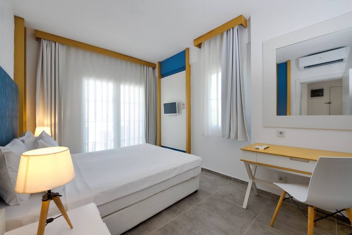 Ein Hotelzimmer mit Bett, Schreibtisch, Stuhl, Lampe und Fernseher.
