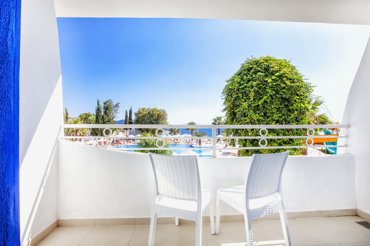 Ein Balkon mit weißen Korbstühlen, einem Pool und Blick auf den Strand.